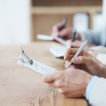 Cropped shot of three coworkers sitting at a table and taking notes