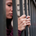 Close up of a female prisoner behind bars. Stress and anxiety showing on her face. Focus on her hands.