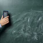 A teacher cleans a dirty green chalkboard