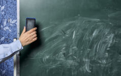 A teacher cleans a dirty green chalkboard