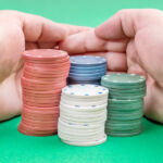 Man hand raking poker chips on green poker table.