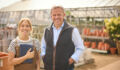 Portrait Of Mature Man And Woman Working Outdoors In Garden Centre Using Digital Tablet