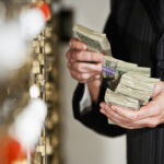 Man holding big stack of US paper currency by safety deposit boxes. Focus on money