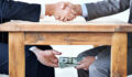 Cropped shot of two businessmen shaking hands while money passes hands under a table