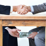 Cropped shot of two businessmen shaking hands while money passes hands under a table