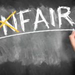hand writes the word unfair and crosses the "un" changing the word to fair on a blackboard