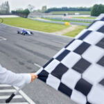 More new data on state of the industry Rear view of auto race official waving chequered flag to blue Formula 1 car driving on track.