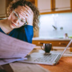 Young female reading documents, using laptop in the kitchen at home