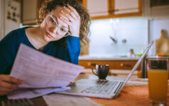 Young female reading documents, using laptop in the kitchen at home
