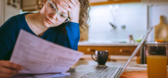 Young female reading documents, using laptop in the kitchen at home