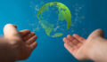A person's outstretched hands pointing the 3D rendered transparent globe with the continents in green on blue background - renewable energy concept