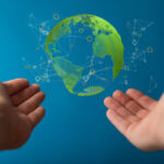 A person's outstretched hands pointing the 3D rendered transparent globe with the continents in green on blue background - renewable energy concept