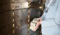 Businesswoman holding big stack of US paper currency, standing by safety deposit boxes