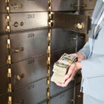 Businesswoman holding big stack of US paper currency, standing by safety deposit boxes
