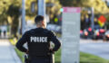 Rear view of an Hispanic police officer patrolling an urban area on foot. He is walking on a sidewalk away from the camera.