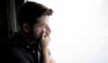 young attractive man looking through window looking worried, depressed, thoughtful and lonely suffering depression in work pressure or personal problems concept with copy space