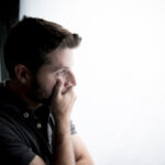 young attractive man looking through window looking worried, depressed, thoughtful and lonely suffering depression in work pressure or personal problems concept with copy space