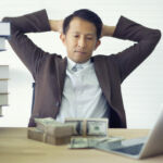 Problems around multiple hats brings $6m penalty Stressed Asian businessman thinking a problem, trouble with money corporate working a difficult assignment in a desktop with stack books on desk.