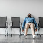 FinCEN seeks your comments on delayed IA AML rule Bored and disappointed male indian employee sitting in waiting room on row of chairs, feeling tired and upset, full length shot, free space
