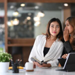 Young business woman whispering in ear of her colleague.