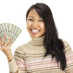 Photo of a smiling young woman with a fan of ten U.S. 100 dollar bills (cash) in her hands; isolated on white. $1000