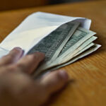 SEC release on residential mortgage-backed securities disclosures Male hand opening a white envelope full of American Dollars (USD, US Dollars) on the wooden table as a symbol of cash transfer, money laundering or bribery