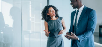 Shot of two young colleagues having a discussion in modern office. Confident young business people working together in the office. Corporate business persons discussing new project and sharing ideas in the workplace.