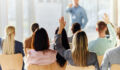 Rear view of a businesswoman raising her hand to ask a question on an education event in board room.