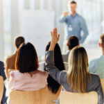 November 3, 2025 RCW Weekly Briefing Rear view of a businesswoman raising her hand to ask a question on an education event in board room.