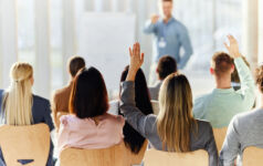 Rear view of a businesswoman raising her hand to ask a question on an education event in board room.