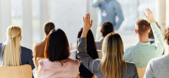 Rear view of a businesswoman raising her hand to ask a question on an education event in board room.