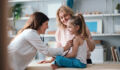 A friendly pediatrician performs a health examination for a happy young girl, observed by her caring mother. The image conveys family care, child health, and professional medical service.