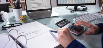 Close-up Of A Businessperson's Hand Calculating Invoice At Workplace