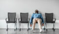 Bored and disappointed male indian employee sitting in waiting room on row of chairs, feeling tired and upset, full length shot, free space