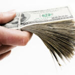 A man's hand holds out a large bundle of US dollars which could be payment, a bribe, or maybe wages. Isolated on white.