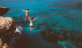 Young active man and woman diving from high cliff into tropical island blue sea water