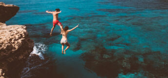 Young active man and woman diving from high cliff into tropical island blue sea water