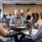 Mature Latin American man going back to school and debating with his classmates - education concepts