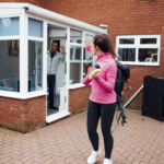 Mid adult woman is waving goobye to her family as she leaves the house to go to the gym.