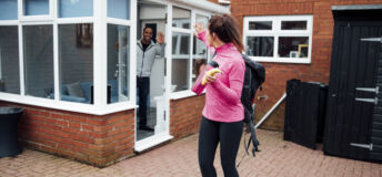 Mid adult woman is waving goobye to her family as she leaves the house to go to the gym.