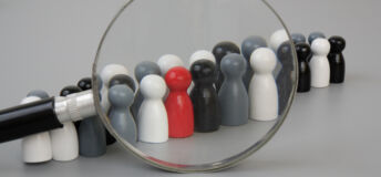 Find talents and review skills concept. Gray, white and black wooden people figures in row and red figure standing out of row under magnifying glass.