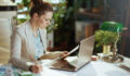 modern woman worker in a light business suit in modern green office with documents and laptop.