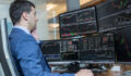 Male stock broker trading online watching charts and data analyses on multiple computer screens.