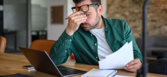 Anxious male financial advisor rubbing eyes while working over laptop and analyzing reports at desk