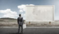 A business man standing and staring at a blank billboard advertisement.