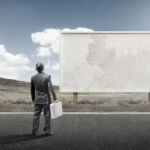 A business man standing and staring at a blank billboard advertisement.
