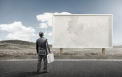 A business man standing and staring at a blank billboard advertisement.