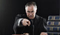 Judge in a legal robe glares at the camera and points with his index finger.