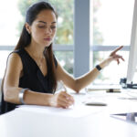 Concentrated professional female journalist making research browsing information for article using computer and wireless connection in office, businesswoman counting profit of company doing report