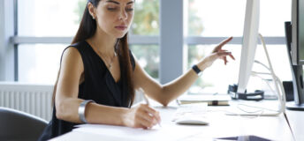 Concentrated professional female journalist making research browsing information for article using computer and wireless connection in office, businesswoman counting profit of company doing report